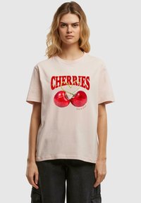 Camiseta de algodón rosa claro con texto grande en rojo "CEREZAS" y gráfico de dos cerezas con tallos verdes, de mangas cortas y corte relajado.