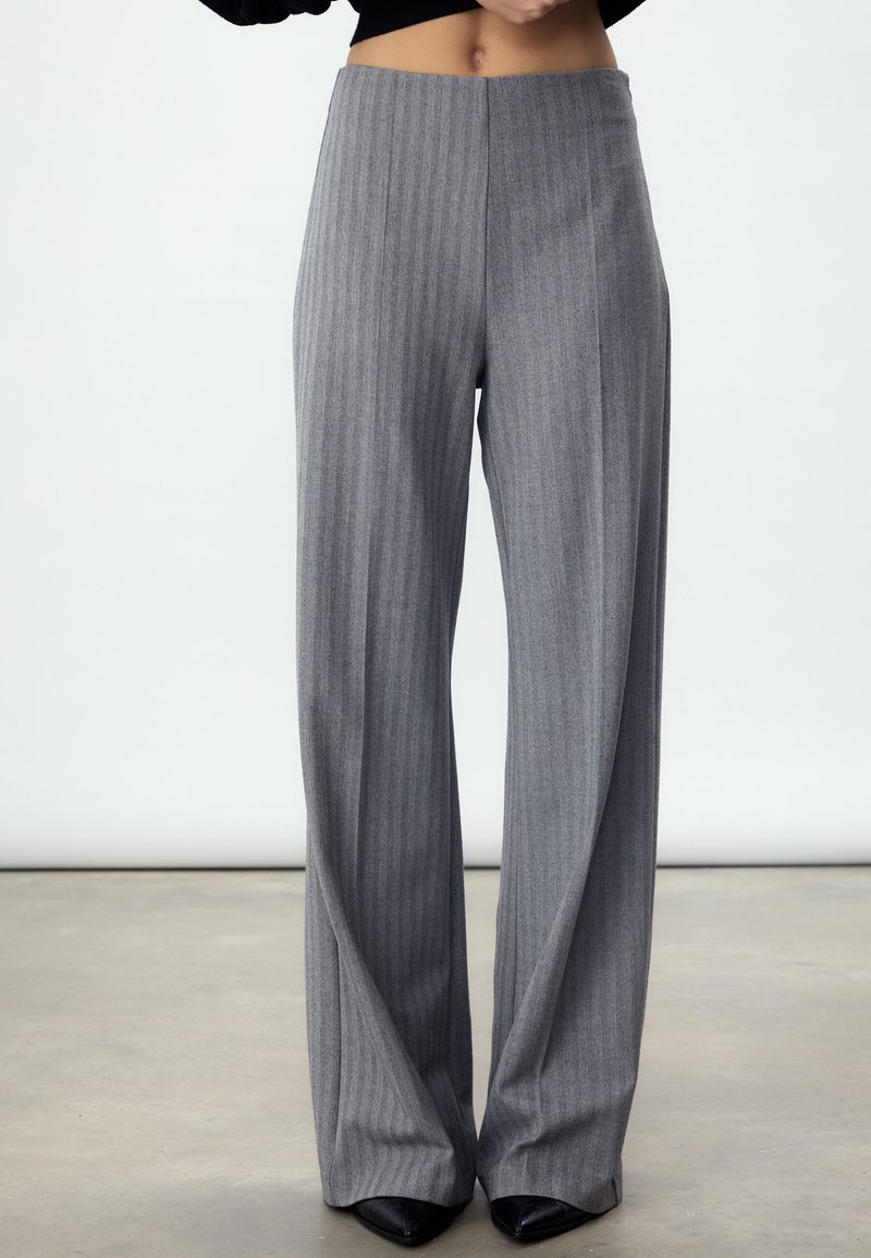 Grijze wijde broekspijpen met krijtstreep en een hoge taille. Zachte stoftextuur en een op maat gemaakt ontwerp, gecombineerd met zwarte pumps met spitse neus.