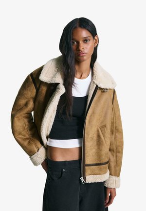 Bruine shearling bomberjack met een crèmekleurige kraag en manchetten, met een ritssluiting en donkere accenten. Draag het over een zwarte top en jeans.