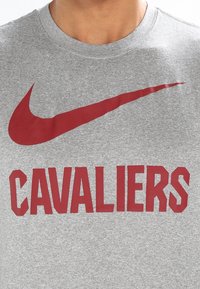 Persona que lleva una camiseta gris con un gran logo de Nike en color rojo encima de la palabra "CAVALIERS" impresa en letras rojas en bloque.