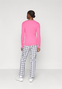 Kohandatud roosa ribasvärk, millel on pikad varrukad, koos musta ja valge ruudulise eritusega pükstega ning valgete kingadega, vaadatuna selja tagant.