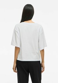 Witte kortekous T-shirt met een relaxed fit, wijde hals, en een zachte textuur, gedragen met zwarte broek, van achteren gezien.