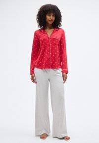 Κόκκινο πάνω μέρος πυτζάμας με λευκή επένδυση και μικρό ανθικό σχέδιο, συνδυασμένο με φαρδιά παντελόνια σε ανοιχτό γκρι. Απαλό ύφασμα και άνετη εφαρμογή.