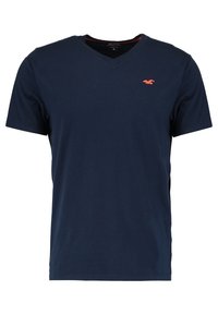 Mörkblå kortärmad V-ringad T-shirt med en liten röd måslogotyp på vänster bröst.