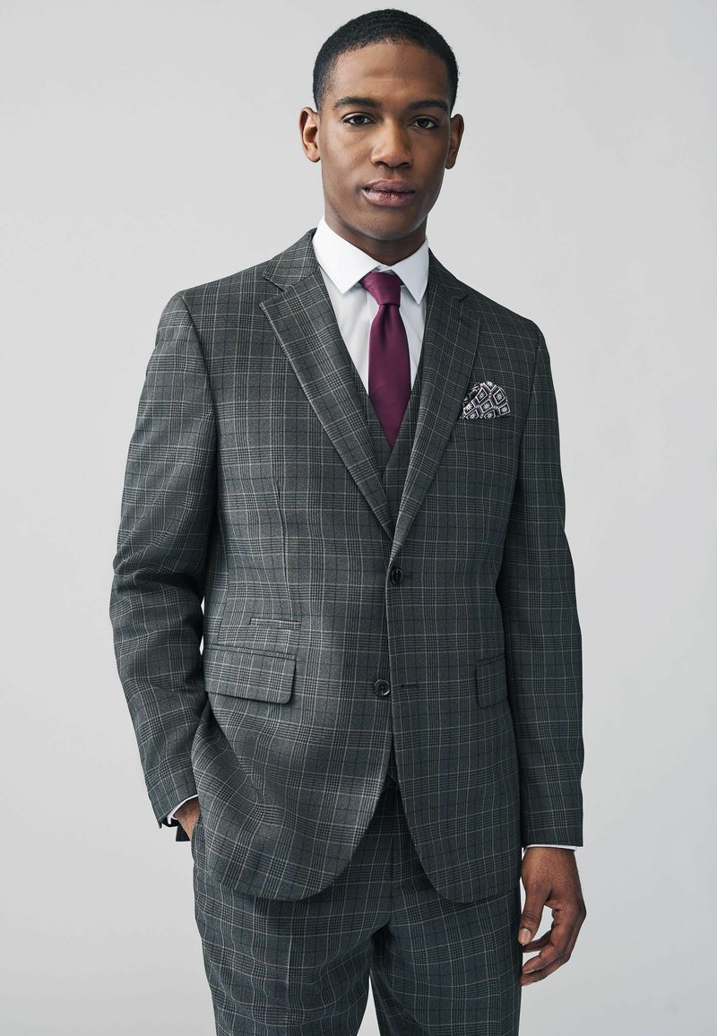 Gray plaid suit with a fitted design, featuring a two-button jacket, white shirt, and a burgundy tie. Pocket square with geometric pattern.