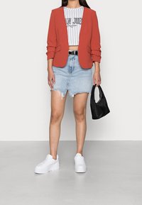 Czerwona marynarka z podwiniętymi rękawami, biały prążkowany top, podkrócony dżinsowy spódniczka, białe platformowe trampki i mała czarna torebka.