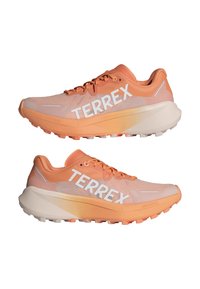 Ľahké oranžové trailové bežecké topánky s sieťovaným zvrškom, gumovou podrážkou a výrazným bielym logom "TERREX" po boku.