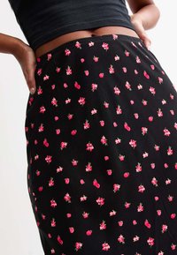 Jupe noire avec un motif floral répétitif de fleurs roses et de fraises. Le tissu semble lisse avec un design ajusté à la taille.