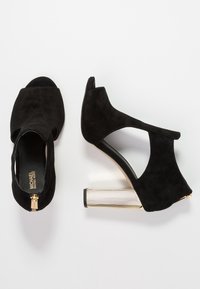 Mustat mokka nilkkurit avoimella varvalla ja leikkauksilla. Varustettu metalliraitaisella palkeella ja vetoketjulla takana.