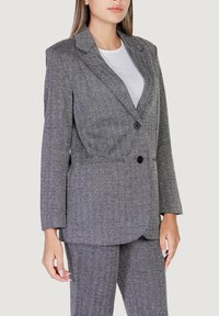 Blazer grigio a spina di pesce con rever a punta, due bottoni neri e una vestibilità rilassata, abbinato a un top bianco a coste.
