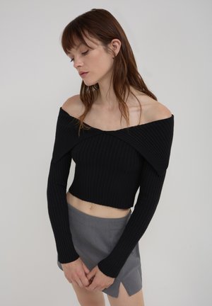 Black ribbed off-shoulder crop top with long sleeves, featuring a unique folded design at the neckline. Paired with a gray mini skirt.