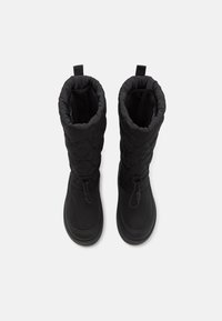 Bottes noires imperméables avec texture matelassée, tige haute et cordon de serrage en haut. Caractéristiques d'une semelle en caoutchouc plate pour une adhérence et une durabilité.