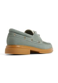 Mocasines para hombre en suave ante verde con punta redondeada, suela de goma contrastante en color marrón y detalles decorativos de costura y cordones.