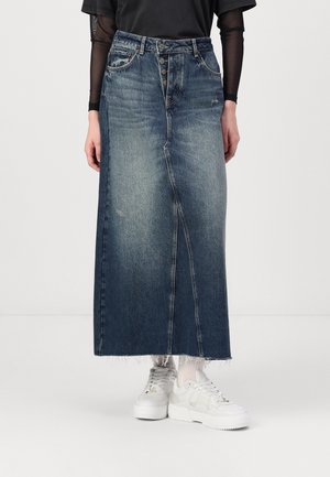 Midilanger blauer Jeansrock mit Knöpfen vorne und rohem Saum, getragen mit weißen Sneakers, weißen Socken und einem schwarzen Top mit transparenten langen Ärmeln.