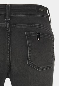 Pantalones vaqueros de mezclilla negra con un diseño clásico de cinco bolsillos, herrajes metálicos y detalles de costura en los bolsillos traseros.
