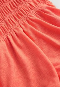 Tissu rose corail avec détail smocké élastiqué créant des motifs texturés et froncés sur un matériau doux et lisse.