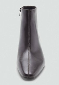 Bottine en cuir noir avec un bout pointu, une texture lisse et une fermeture éclair latérale. Détails de surpiqûre le long de la couture avant.