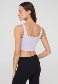 Top cropped color lilla con spalline larghe e scollatura quadrata, realizzato in tessuto liscio e elasticizzato. Abbinato a leggings neri.