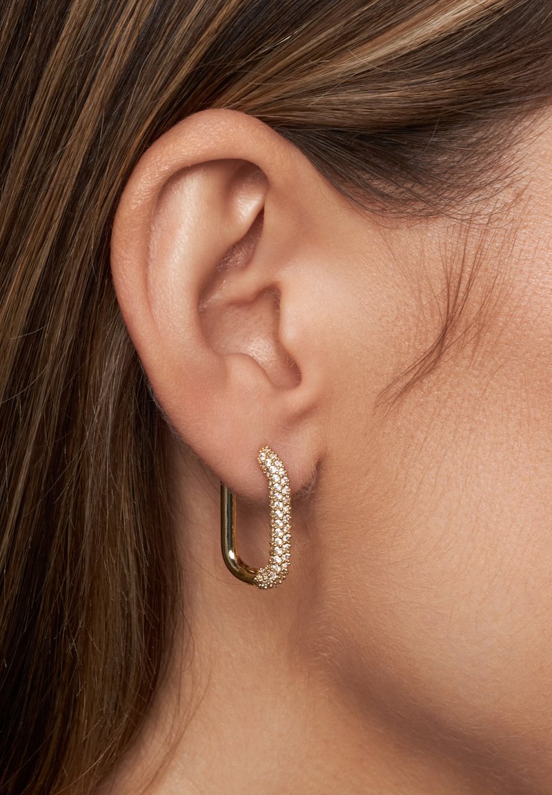 Boucles d'oreilles en or en forme de hoops avec un design incurvé et texturé, ornées d'une rangée de petits cristaux transparents le long d'un bord, mettant en valeur une finition métallique élégante.