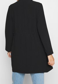 Cappotto nero a maniche lunghe con vita a cintura e taglio dritto. Tessuto liscio con un design minimale e senza hardware o motivi visibili.