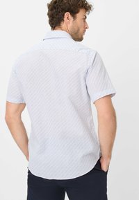 Camicia a maniche corte di colore azzurro chiaro con un piccolo motivo geometrico ripetuto. Presenta una texture morbida e un orlo curvo sul retro.
