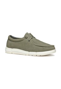 Zapatos de lona verdes sin cordones con punta redonda, suela blanca de goma y detalles de costura mínimos. Construcción flexible para mayor comodidad.