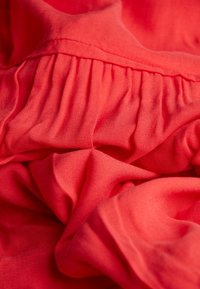 Roter Stoff mit weicher, glatter Textur und Falten. Das Material wirkt leicht und fällt locker, wobei es eine lebendige Farbe zur Schau stellt.