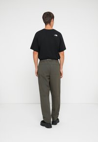 Sort bomulds t-shirt med et lille hvidt logo på ryggen, sat sammen med olivengrønne cargo bukser med flere lommer og en afslappet pasform.