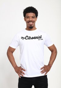 Bílý bavlněný tričko s černým textem "The Citroënist Est. 1919" ve výrazném kurzívním písmu. Krátké rukávy a standardní kulatý výstřih.