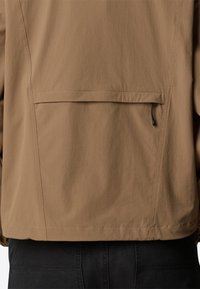 Brown lightweight jacket with a smooth texture, featuring a back pocket with a drawcord and seam detailing, designed for functionality.