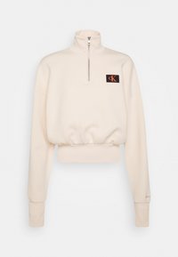 Kremowy, krótki podkoszulek z wysokim zamkiem, prążkowane mankiety i czarna naszywka z pomarańczowym logo cK.