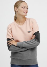 Sweatshirt coloré en blocs rose et gris avec un col rond, des poignets côtelés, et un patch logo sur la poitrine. Tissu doux avec une coupe décontractée.
