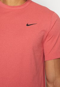 Camiseta roja de manga corta con textura, cuello redondo y un logo negro de Nike en la parte superior izquierda del pecho.