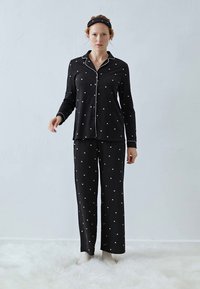Svart pyjamas med små vita hjärtan, bestående av en skjorta med krage och knäppning samt långa byxor. Slät tyg och avslappnad passform.