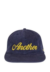 Jūras spēku zila korduroja snapback cepure ar dzeltenu izšūtu tekstu "Another" priekšpusē. Plakans vizieris ar teksturētu auduma virsmu.