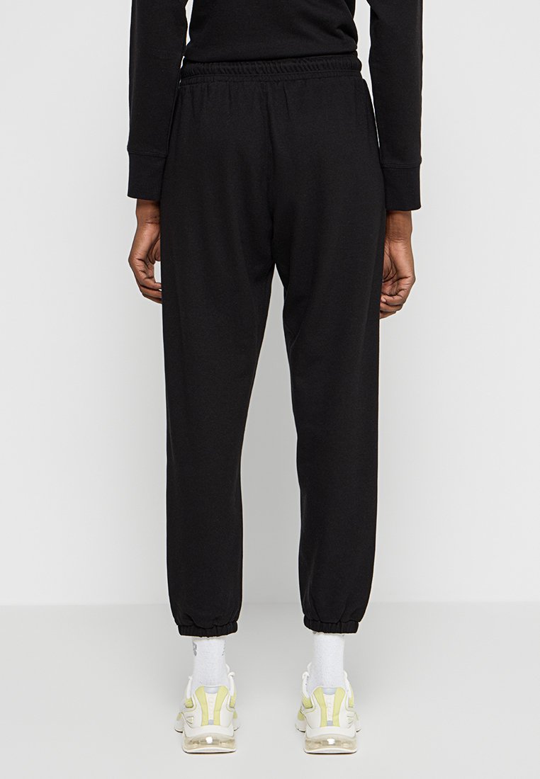 Czarne dresy z elastycznym pasem, zwężanymi mankietami i gładką fakturą, połączone z białymi i żółtymi trampkami.