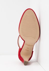 Chaussure à talon pour femme en daim rouge positionnée à la verticale montrant la semelle avec la marque Gabor, taille 4½, et l’étiquette "Made in Portugal".