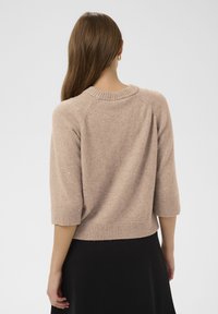 Rövid ujjú, bézs színű kötött pulóver bordázott szegéllyel és gallérral, finom csillogással a háton. Puha, texturált anyag.