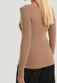 Brun ribbad tröja med långa ärmar, med en figursydd design och ett texturerat tyg. Baksidan har en diskret rundad halsringning.