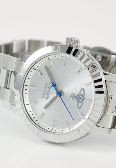 Relógio de aço inoxidável prateado com mostrador escovado, ponteiros azuis e gravação "Vivienne Westwood". Apresenta uma bracelete metálica e bisel estriado.