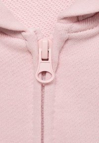 Giacca con cerniera di colore rosa chiaro, realizzata in tessuto a maglia morbido, con cerniera e colletto coordinati. Il tessuto appare traspirante e liscio.