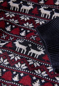 Stickad tröja med en mörkblå botten och mönster i rött, vitt och marinblått, inklusive renar, träd och geometriska former. Ribbad mudd.