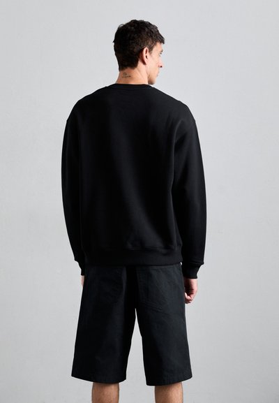 Svart tröja med ribbad mudd och nederkant, i kombination med svarta shorts med en strukturerad design och sidofickor. En enkel, stilren look.