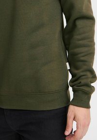 Oliven grøn sweatshirt lavet af blødt materiale, med ribbede manchetter og kant, samt et lille mærke på siden.