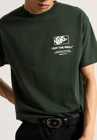 Camiseta de algodón verde con el logotipo blanco de Vans y el texto "OFF THE WALL", cuello redondo, mangas cortas y un ajuste suave y casual.