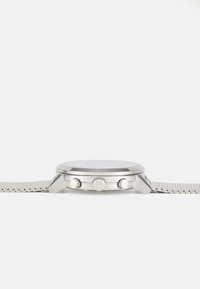Reloj plateado con esfera redonda, correa de malla, dos botones de corona y diseño minimalista. Textura suave y acabado metálico sólido.