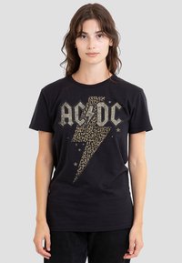 Schwarzes Baumwoll-T-Shirt mit Leopardenmuster und einem Blitz in Grau, dazu der Text "AC/DC" mit Sternakzenten. Kurze Ärmel und Rundhalsausschnitt.