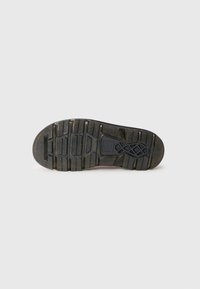 Rubber shoe sole, black with textured surface, featuring grooves for traction, reinforced sections, and a distinctive logo pattern.