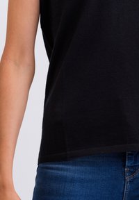 Top nero a maniche corte realizzato in un tessuto morbido, con una vestibilità rilassata e orlo dritto, abbinato a jeans blu denim.
