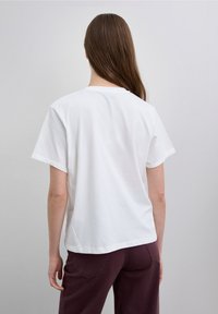 White cotton t-shirt with a crew neck and short sleeves, relaxed fit, smooth texture, paired with dark purple pants.